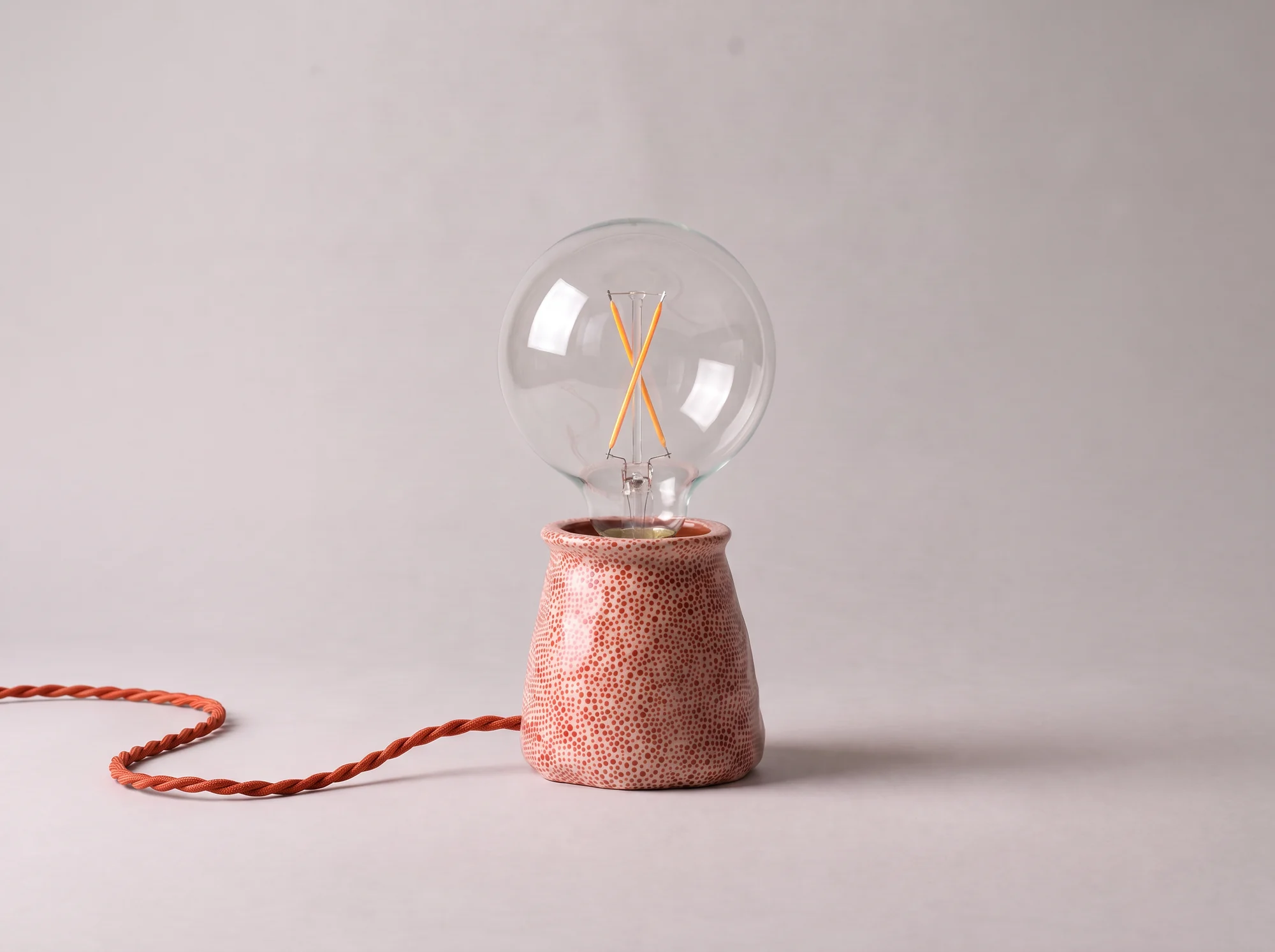 Lampa Kona Dots stinsă: corp din lut roz cu buline roșii, bec cu filament și cablu textil răsucit